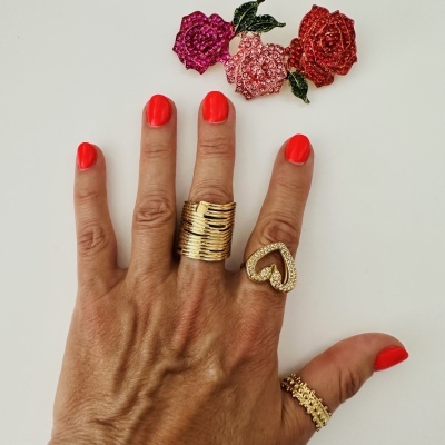 Mão com unhas vermelhas e vários anéis dourados e broche de flores brilhantes