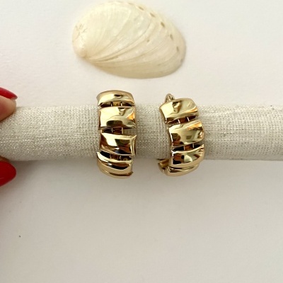 Brincos dourados com design em camadas texturizadas em suporte de tecido bege