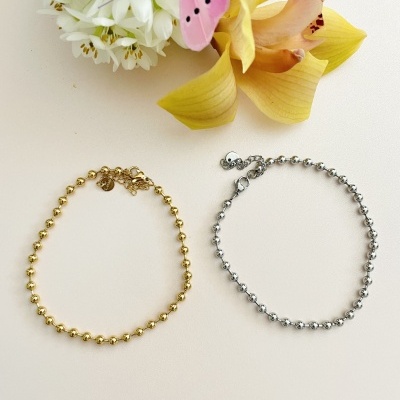 Dois colares de bolas pequenas, dourado e prateado, com flores ao fundo