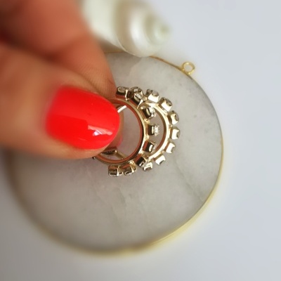 Anel metálico dourado com detalhes em forma de engrenagem numa superfície branca circular.