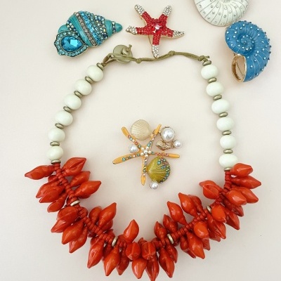 Colar de contas brancas e pendentes vermelhos com broches de conchas e estrelas do mar coloridas