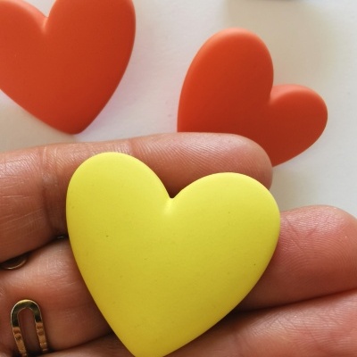 Quatro corações de silicone ou borracha coloridos em fundo branco, sendo um amarelo na mão.