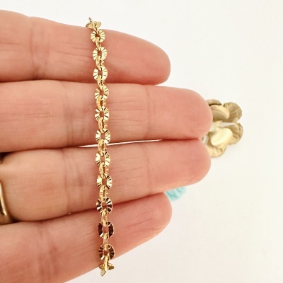 Pulseira dourada com elos circulares texturizados numa mão