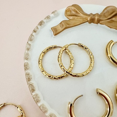 Brincos de argola dourados numa bandeja branca com laço dourado