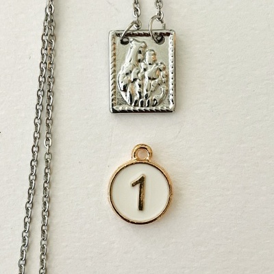 Colar com dois pendentes, um quadrado prateado com relevo e outro redondo com o número 1.