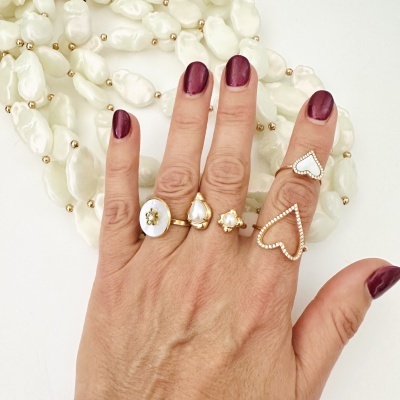 Mão com vários anéis dourados e colares de contas brancas no fundo branco.