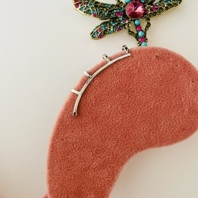 Libélula colorida sobre superfície rosa aveludada com peça metálica prateada