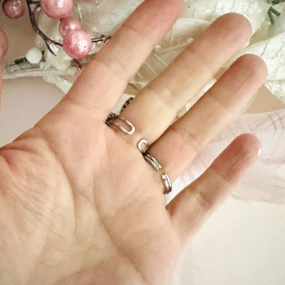 Anel aberto prateado na mão com frutos cor-de-rosa e folhas brancas ao fundo