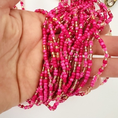 Pulseiras de contas cor de rosa e douradas nas mãos com fundo branco