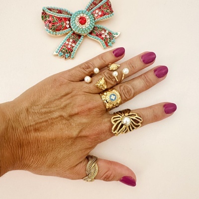 Mão com anéis dourados e broche vermelho em fundo bege