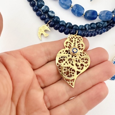 Pulseira com contas azuis e pendentes dourados com desenho de pássaro e folha em filigrana na mão
