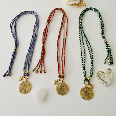 Três pulseiras trançadas com medalhões dourados, pendente de coração branco, flor branca e broche em coração dourado com pérolas.