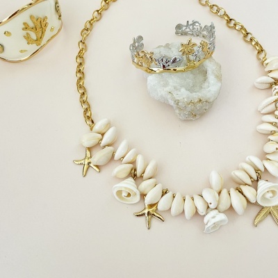 Colar e anel decorativos com motivos marinhos sobre fundo bege claro