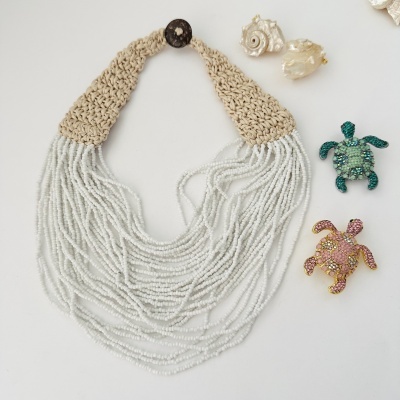 Colar branco com tecido trançado bege e pendentes de tartarugas decorativas coloridas sobre fundo branco