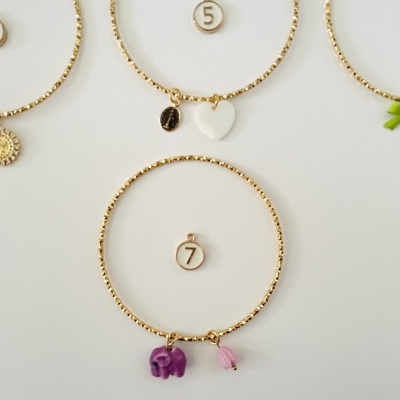 Pulseiras douradas com pendentes e números 5 e 7 em círculos brancos