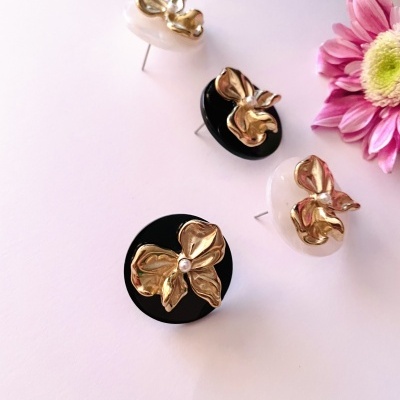 Brincos redondos com flores douradas sobre bases pretas e brancas
