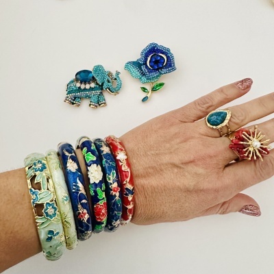 Pulseiras e anéis florais em esmalte e metal dourado, com broches elefante e flor azul.