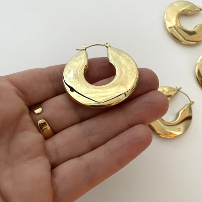 Argolas douradas de formato irregular e textura ondulada na mão