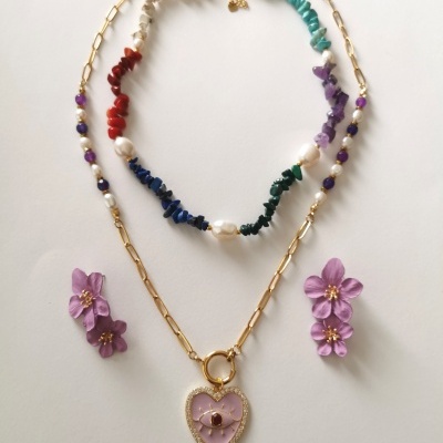 Conjunto de dois colares coloridos e três flores roxas artificiais sobre fundo branco.