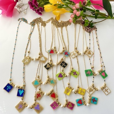 Colares dourados com pingentes quadrados coloridos e flores ao fundo