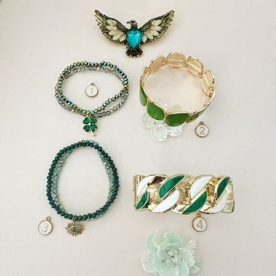 Conjunto de bijuterias: broche de pássaro, duas pulseiras de contas verdes, pulseira dourada com detalhes verdes, pulseira dourada larga com verdes e broche flor verde.