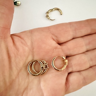 Três pares de brincos argola dourados na palma da mão