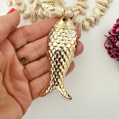 Colar com contas brancas e pendente de peixe dourado segurado por mão feminina
