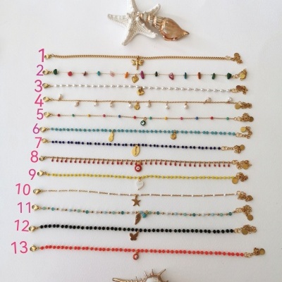 Conjunto de 13 pulseiras douradas com contas coloridas e pingentes, dispostas em fundo branco com conchas decorativas