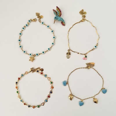 Pulseiras e broche de joalharia colorida e dourada em fundo branco