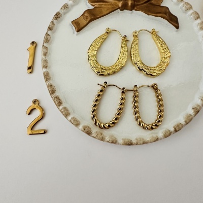 Brincos dourados com texturas em prato branco com bordas castanhas e números dourados ao lado