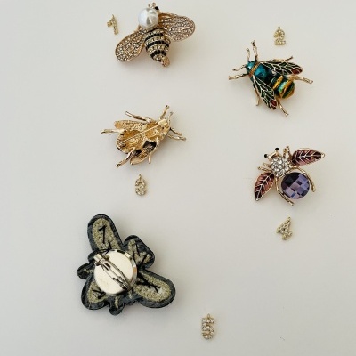 Pins decorativos em forma de abelhas com detalhes metálicos e pedras coloridas em fundo branco