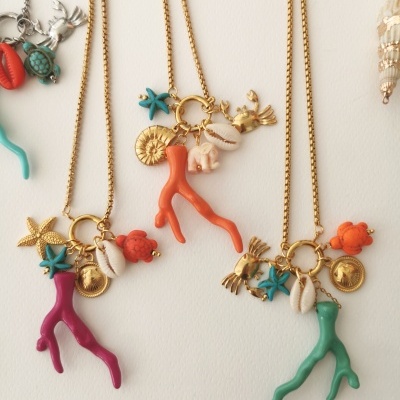 Colares com pendentes de corais, conchas, estrelas-do-mar e medalhões, em fundo branco.
