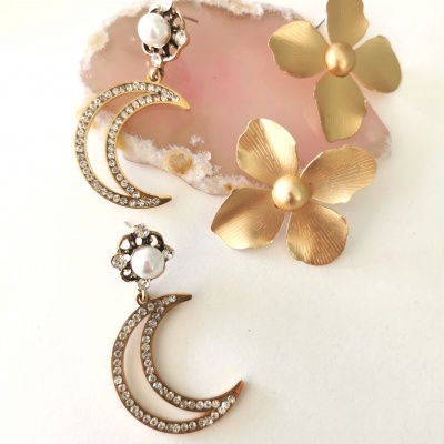 Brincos com forma de lua, pérolas e cristais sobre pedra rosa e flores douradas