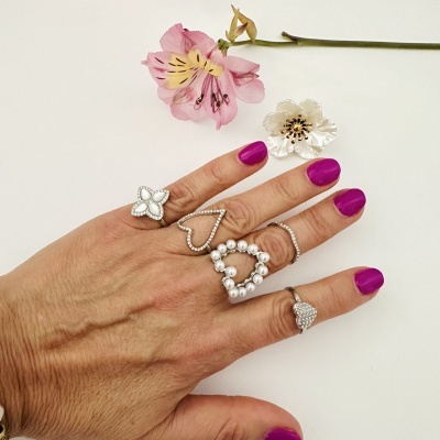 Mão com anéis de prata, unhas roxas e flores artificiais rosa e branca sobre fundo branco