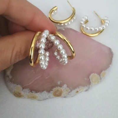 Conjunto de brincos e anelar com dourado e pérolas sobre pedra rosa.