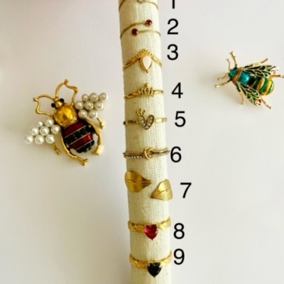 Anéis dourados numerados e broches de abelhas em fundo branco