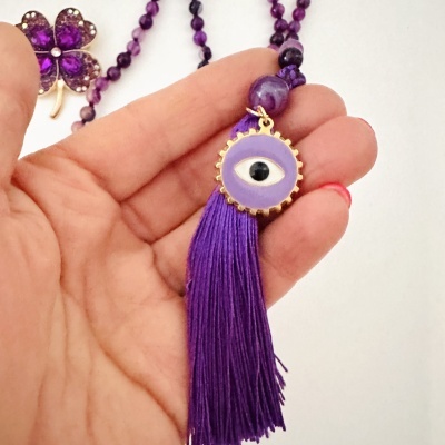 Colar roxo com pendente de olho e franjas, broche de flor roxa ao fundo