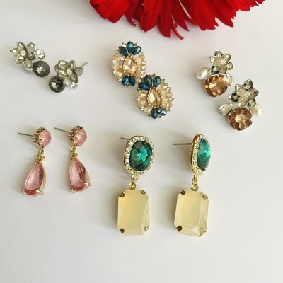 Cinco pares de brincos variados com pedras coloridas e pérolas sobre fundo branco