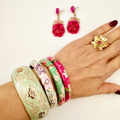 Pulseiras e anel florais em verde, rosa e dourado com brincos pendentes rosa em mão feminina