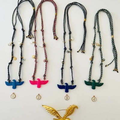 Quatro colares com pendentes de pássaros coloridos e um broche dourado em forma de ave.