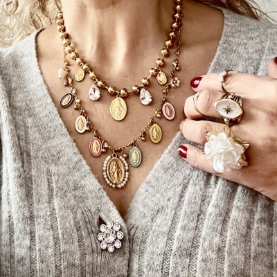 Colares e anéis dourados com pendentes, broche com pedras em casaco cinza, mão com unhas vermelhas