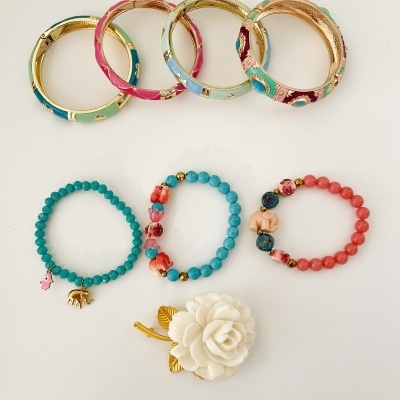Pulseiras coloridas e broche flor branca com folhas douradas sobre fundo branco