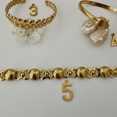 Pulseiras douradas e pendentes com números sobre fundo branco