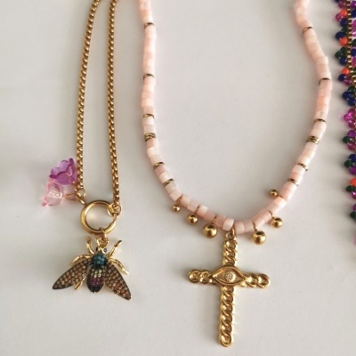 Dois colares, um com pendente de abelha colorida e outro com cruz dourada e contas cor-de-rosa.