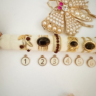 Conjunto de anéis dourados com pedras preto e vermelho e broche dourado em forma de inimigo com pérolas