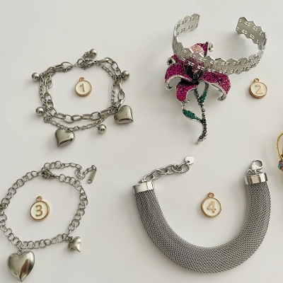 Conjunto de pulseiras metálicas prateadas e um adorno floral cor-de-rosa sobre fundo branco