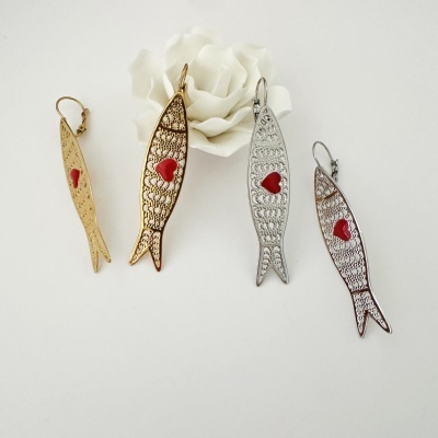Quatro brincos em forma de peixe, dourados e prateados, com coração vermelho e filigrana, sobre fundo branco com flor branca.