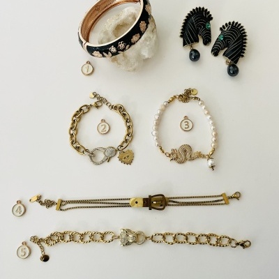 Conjunto de pulseiras e brincos femininos com etiquetas numeradas, pulseira rígida preta e cobre, brincos leque pretos, três pulseiras douradas e brancas sobre fundo branco.