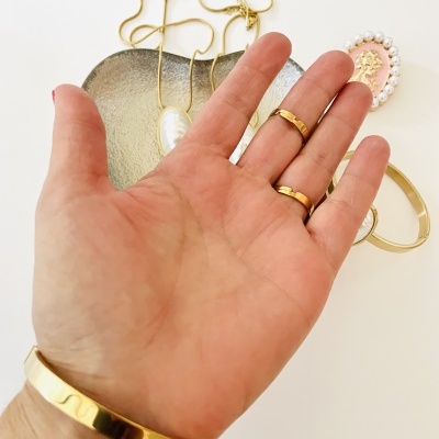 Mão com pulseira e anéis dourados, colar, bracelete e broche no fundo