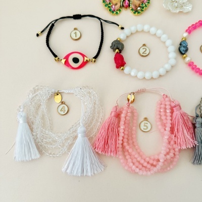 Cinco pulseiras numeradas com contas e franjas em várias cores num fundo bege claro